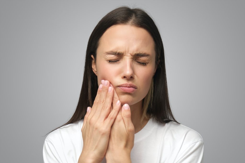 Miserable woman experiencing severe toothache, pressing palm to cheek, closing eyes because of pain