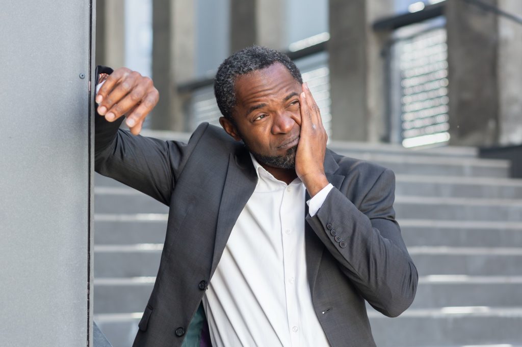 Toothache on the street. A senior African American man in a suit stands outside an office and holds