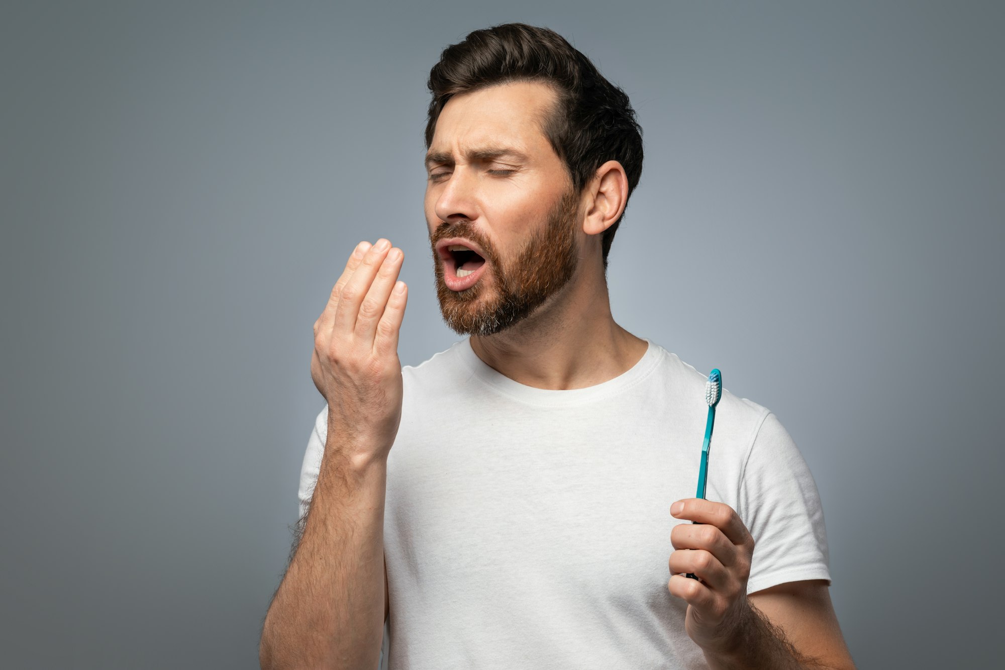 Bad breath. Handsome middle aged man checking his breath with his hand, blowing to it, standing over